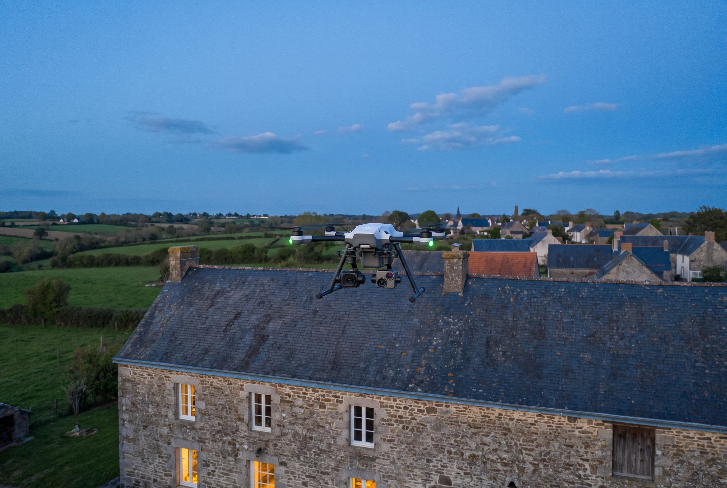 Image d'illustration : drone d'inspection au-dessus du toit d'une longère, à la tombée du jour